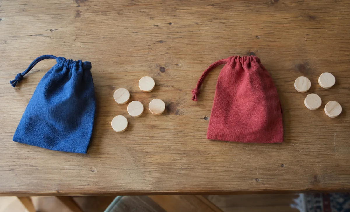 Deux sacs de couleurs différentes sont placés près de jetons en bois.