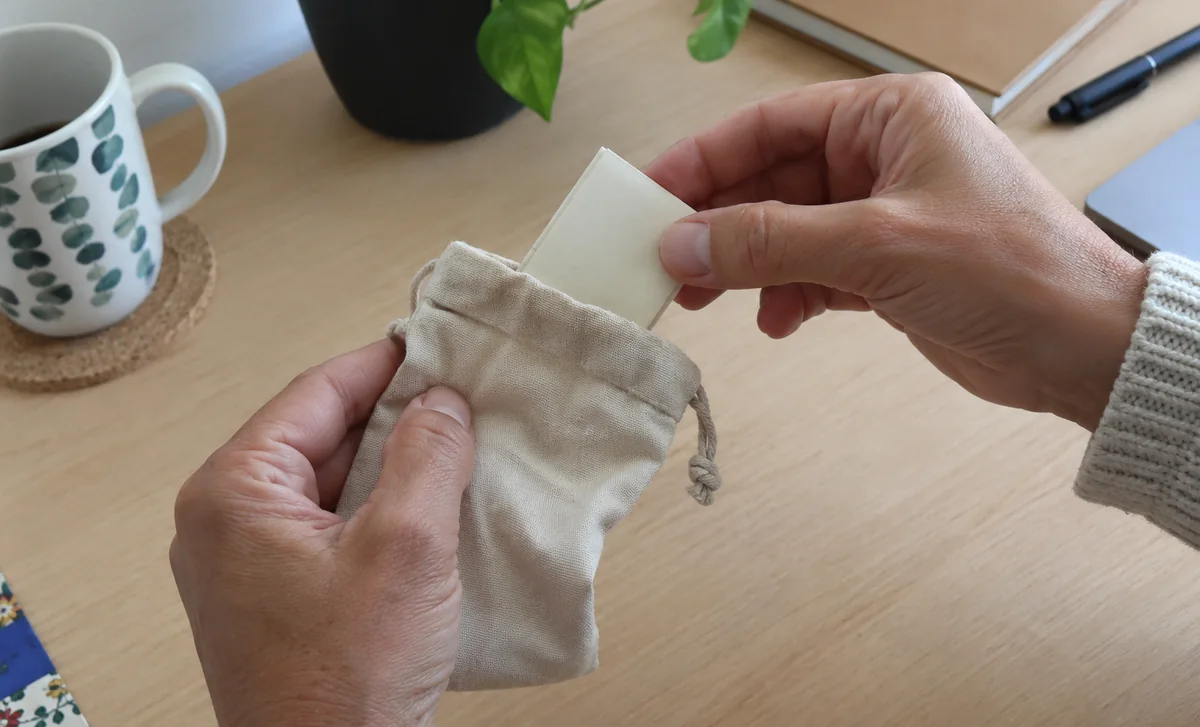 Des mains tirent un papier plié dans un sac en tissu.
