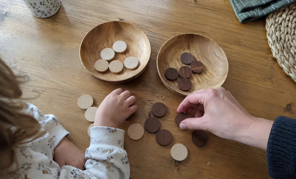 Des mains d’adulte et d’enfant déplacent des jetons près de deux bols en bois.